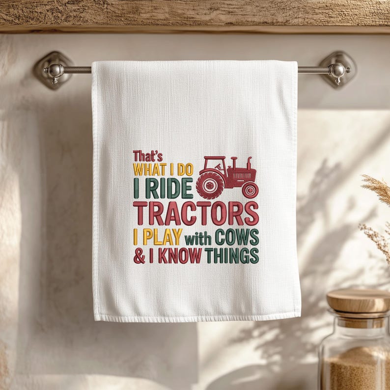 Peut inclure: Serviette de cuisine blanche avec le texte "That's What I Do, I Ride Tractors, I Play with Cows & I Know Things" en vert, rouge et jaune. Un dessin de tracteur rouge est &eacute;galement inclus.