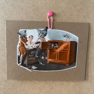 Puede incluir: Un collage de medios mixtos con una ilustración vintage de una escena familiar con cabezas de gato reemplazando cabezas humanas. La escena se mantiene unida con un clip rosa. La familia está reunida alrededor de un mueble de madera con un tocadiscos.