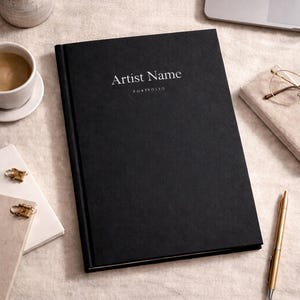 Pu&ograve; includere: Un portfolio con copertina rigida nera e il testo Artist Name e PORTFOLIO stampato in bianco sulla copertina anteriore. Il libro ha una finitura testurizzata ed &egrave; posizionato centralmente, con un design pulito per conservare opere d'arte.