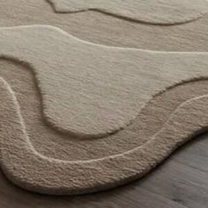 Pu&ograve; includere: Un tappeto beige e marrone chiaro con un design topografico a strati. Il tappeto presenta un motivo ondulato e organico con diverse tonalit&agrave; di beige e marrone chiaro, creando un effetto strutturato e tridimensionale. Il design del tappeto assomiglia a un paesaggio.