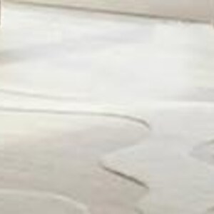 Pu&ograve; includere: Un tappeto beige chiaro, di forma astratta, con un design ondulato e organico. Il tappeto &egrave; posizionato su un pavimento in legno chiaro, con uno scorcio di una gamba del divano nell'angolo in alto a sinistra. I bordi del tappeto hanno un bordo pi&ugrave; scuro e contrastante.