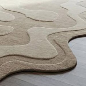 Pu&ograve; includere: Un tappeto beige e marrone chiaro con un design unico a strati. Il tappeto presenta un motivo fluido e organico con diverse tonalit&agrave; di beige e marrone chiaro, creando un effetto strutturato e tridimensionale. Il tappeto &egrave; realizzato in un materiale morbido.