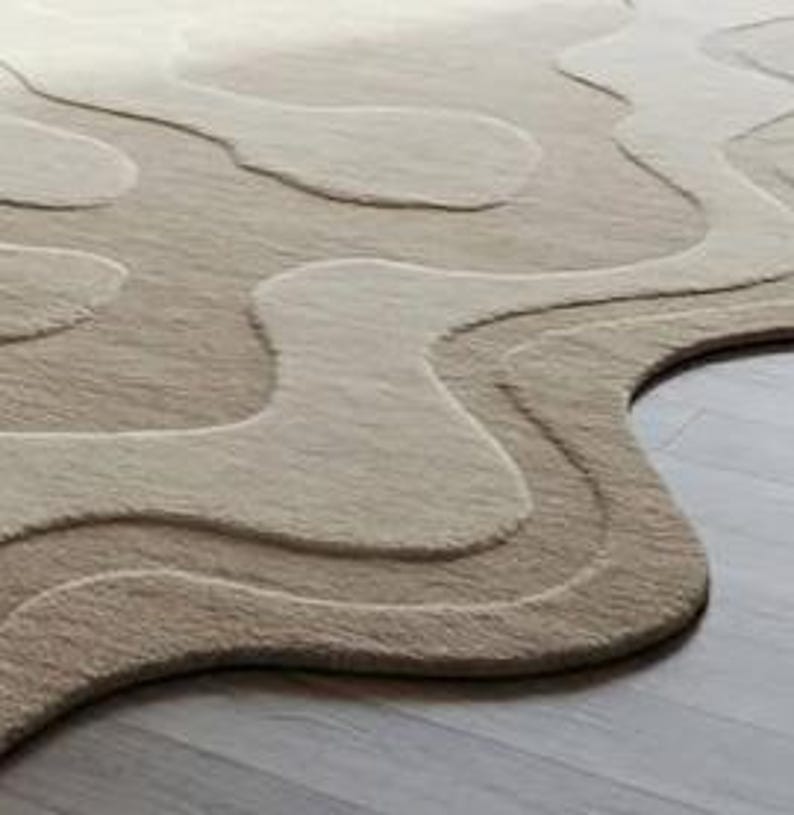 Pu&ograve; includere: Un tappeto beige e marrone chiaro con un design unico a strati. Il tappeto presenta un motivo fluido e organico con diverse tonalit&agrave; di beige e marrone chiaro, creando un effetto strutturato e tridimensionale. Il tappeto &egrave; realizzato in un materiale morbido.