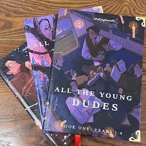 May include: Three hardcover books with illustrated covers. The book covers feature illustrations of young people in a train car, with the title "ALL THE YOUNG DUDES" and "BOOK ONE: YEARS 1-4". A red ribbon bookmark is visible.