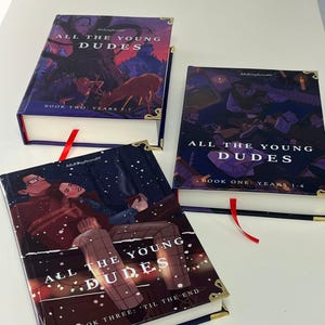 May include: Three hardcover books titled "ALL THE YOUNG DUDES" with different cover illustrations. Each book has a red ribbon bookmark and gold-colored corner protectors. The book covers feature illustrations with dark color schemes and text.