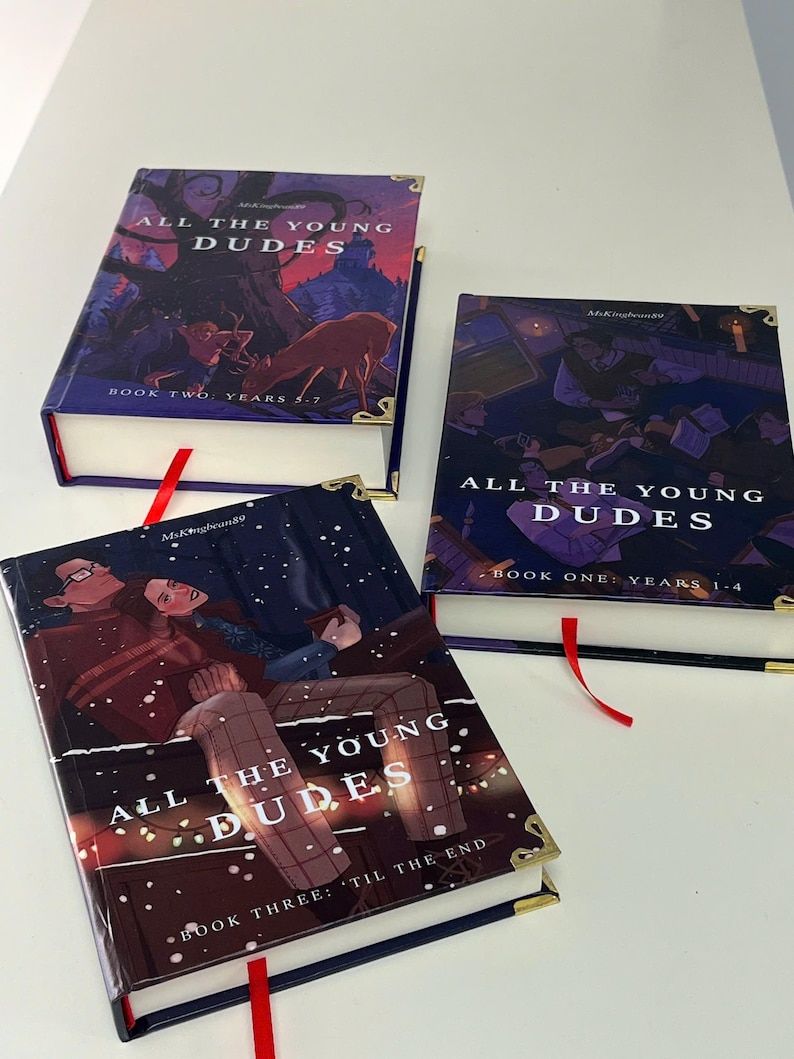 May include: Three hardcover books titled "ALL THE YOUNG DUDES" with different cover illustrations. Each book has a red ribbon bookmark and gold-colored corner protectors. The book covers feature illustrations with dark color schemes and text.