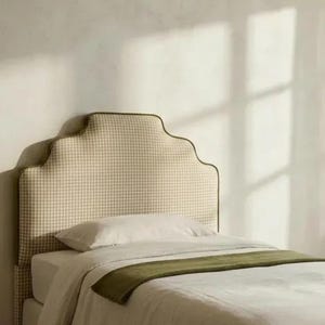 May include: A bed with a patterned headboard and a green throw blanket. The headboard has a scalloped top and is covered in a beige and white gingham fabric. The bed has white linens.