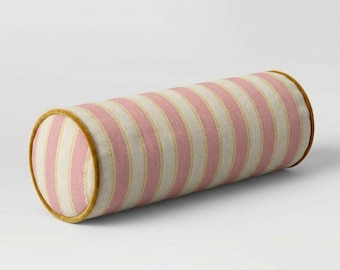 Puede incluir: Un cojín cilíndrico con rayas verticales en tonos alternos de rosa suave y blanco roto. Los extremos y los bordes del cojín están rematados con un ribete de color amarillo mostaza sólido que perfila la forma circular del objeto.