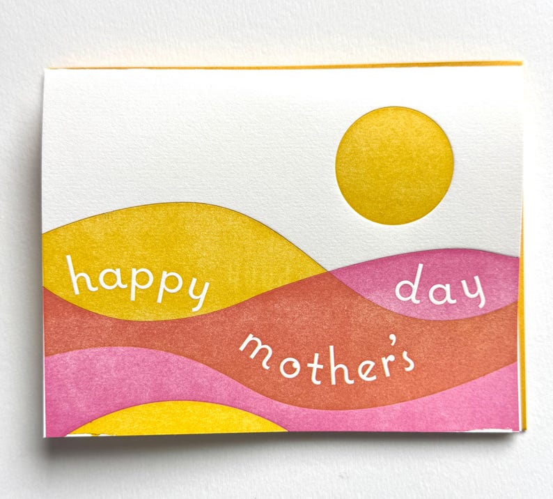 Puede incluir: Una tarjeta de felicitaci&oacute;n del D&iacute;a de la Madre con un sol amarillo y bandas onduladas superpuestas de amarillo, naranja y rosa. Las palabras "happy mother's day" est&aacute;n escritas en blanco. La tarjeta es rectangular con fondo blanco y borde amarillo.