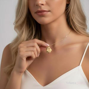 Peut inclure: Un collier pendentif en or avec un design abstrait en couches. Le pendentif est tenu par une personne. Le collier a une chaîne délicate. Le pendentif mesure environ 2 cm de long.