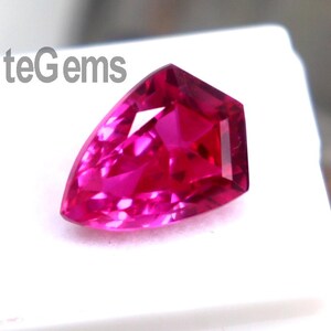 May include: A faceted, hot pink gemstone with a unique, asymmetrical shape. The gem is set on a white surface, with the text "EliteGems" visible. The gemstone's vibrant color and cut create a striking visual appeal.