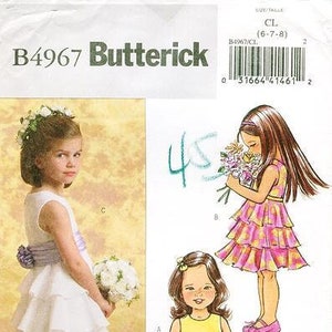 May include: A sewing pattern for two girls' dresses. The pattern is for sizes 6-7-8. The first dress is a white, tiered dress with a yellow sash. The second dress is a pink, tiered dress with a floral print.