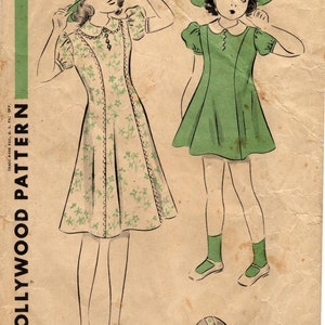 May include: Vintage sewing pattern illustration featuring two young girls in dresses and hats. One dress is cream with green floral accents, the other is solid green. The pattern is for 6 years old and is a Hollywood Pattern.