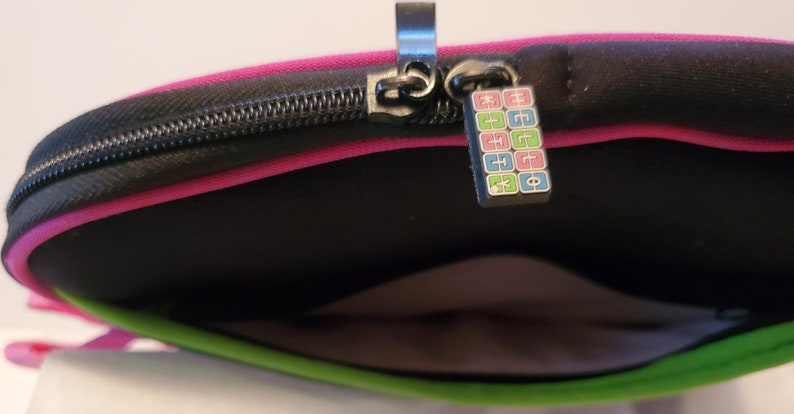 Pu&ograve; includere: Una custodia per laptop rosa e verde con una cerniera nera e un tiretto della cerniera colorato con il testo "EGGO" su di essa.