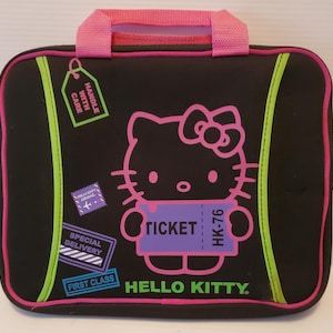 Pu&ograve; includere: Custodia per laptop nera con un design Hello Kitty. La custodia ha una maniglia rosa, un bordo verde e un biglietto viola con il testo "TICKET HK-76".