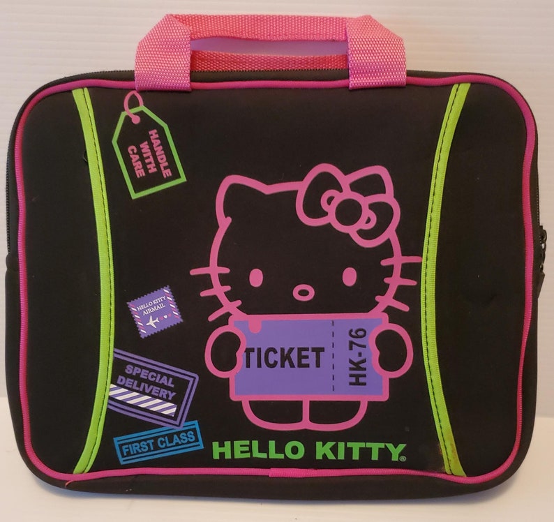 Pu&ograve; includere: Custodia per laptop nera con un design Hello Kitty. La custodia ha una maniglia rosa, un bordo verde e un biglietto viola con il testo "TICKET HK-76".