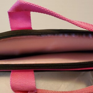 Pu&ograve; includere: Una custodia per laptop di colore rosa e nero con chiusura a zip e interno imbottito. La custodia ha una maniglia superiore e due maniglie laterali.