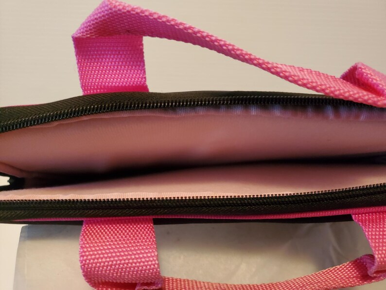 Pu&ograve; includere: Una custodia per laptop di colore rosa e nero con chiusura a zip e interno imbottito. La custodia ha una maniglia superiore e due maniglie laterali.