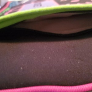 Pu&ograve; includere: Primo piano di una tasca nera con cerniera su una borsa con motivo verde e rosa. La tasca &egrave; foderata con un tessuto grigio chiaro.