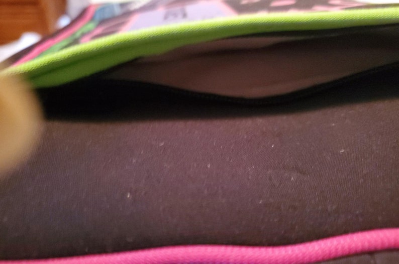 Pu&ograve; includere: Primo piano di una tasca nera con cerniera su una borsa con motivo verde e rosa. La tasca &egrave; foderata con un tessuto grigio chiaro.