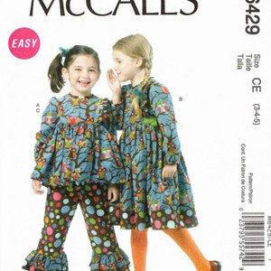 May include: A sewing pattern for a girl's dress and pants. The pattern is for sizes 3-4-5. The dress has a blue and brown owl print and the pants have a colorful polka dot print. The pattern is from McCall's and is labeled "Easy".