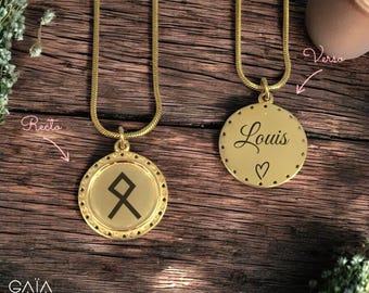 Op de afbeelding: Twee goudkleurige hangerkettingen met bijpassende kettingen. Eén hanger heeft een zwart rune-symbool, de andere heeft de naam "Louis" en een hartsymbool. De hangers liggen op een houten oppervlak.