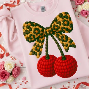 Può includere: Una felpa rosa chiaro con un grande fiocco e un design a ciliegia. Il fiocco ha un motivo leopardato nei toni del marrone e del giallo. Due ciliegie rosse pendono sotto. La felpa è decorata con nastri rossi e bouquet di rose.