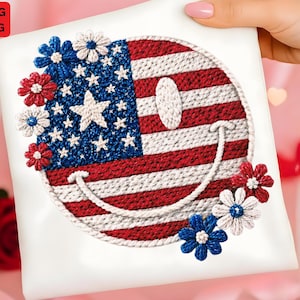 May include: A white square with a smiling face design, incorporating the American flag. The design features red and white stripes, blue stars, and white embroidered flowers. The design is held by a person.
