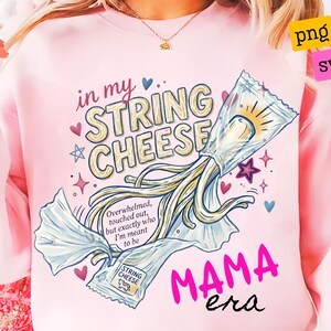 Puede incluir: Una sudadera rosa claro con un gráfico de un palito de queso parcialmente desenvuelto. El texto dice in my STRING CHEESE, Overwhelmed, touched out, but exactly who I'm meant to be, y MAMA era. Pequeños corazones y estrellas rodean el diseño.