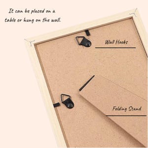 May include: Back of a wooden picture frame with a folding stand and wall hooks. The text says, "It can be placed on a table or hung on the wall."