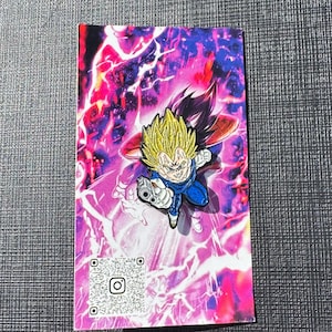 以下が含まれることがあります： 黄色いとがった髪と青い衣装のキャラクターが武器を持っているカラフルなピン。ピンはピンクと紫のエネルギーの活気のある背景に設定されています。QRコード付きのカードが見えます。