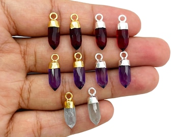 Puede incluir: Una colección de colgantes de piedras preciosas en varios colores, incluyendo rojo intenso, púrpura y transparente. Cada colgante tiene una forma alargada y facetada y está rematado con un lazo de metal dorado o plateado para colgar.