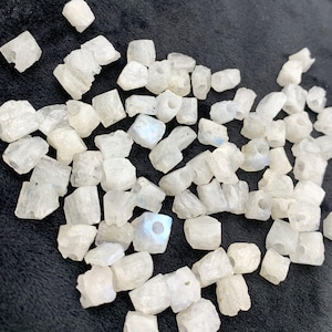 May include: A collection of raw, white moonstone beads with a slightly translucent appearance. The beads are irregularly shaped and have a natural, unpolished look. Some beads show a subtle play of color, and each bead has a hole for stringing.