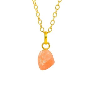May include: A gold-colored chain necklace with a peach-colored, irregularly shaped pendant. The pendant is suspended from a small gold loop. The chain is made of oval links. The background is white.