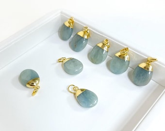 Può includere: Una collezione di pendenti in pietra acquamarina con cappucci e anelli color oro. I pendenti sono di forma ovale e di dimensioni variabili. Sono esposti in un vassoio bianco, che mette in risalto il loro colore verde-azzurro pallido.