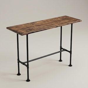 May include: A rectangular console table featuring a dark brown stained wooden top with visible grain patterns. The table is supported by a black metal frame constructed from industrial pipes, including four vertical legs and a horizontal support bar.
