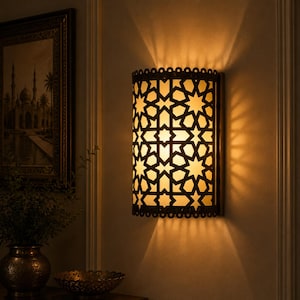May include: A semi-cylindrical wall sconce featuring a dark metal frame with an intricate geometric star pattern. The fixture emits a warm, diffused glow, casting sharp, radiating light patterns onto the wall above and below the unit.