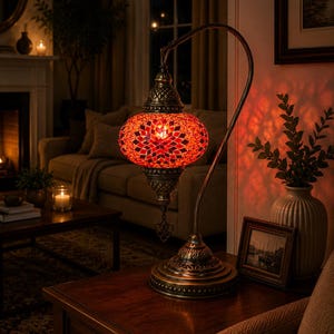 Könnte beinhalten: Eine Tischlampe mit einem geschwungenen, bronzefarbenen Metallständer und einem kugelförmigen Lampenschirm aus kleinen, bunten Glasplättchen in Rot- und Orangetönen, die ein geometrisches Sternmuster bilden und ein warmes Licht ausstrahlen.