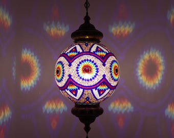 May include: A hanging, spherical mosaic lamp with a dark bronze finish. The lamp features a colorful, intricate pattern of red, yellow, blue, and white glass. The lamp is suspended by a chain and casts a patterned light on the wall.