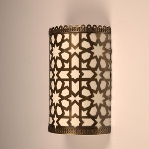 May include: A semi-cylindrical wall sconce featuring a metallic bronze-toned frame with an intricate, laser-cut geometric star and polygon pattern. The frame overlays a white, translucent panel that diffuses light, with scalloped edges.