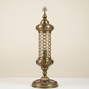 以下が含まれることがあります： ハニカム模様の円筒形ガラスボディを備えた装飾的な真鍮ランプ。 ランプには、花の模様や装飾的な飾りなど、精巧なディテールが施されています。 ベースは丸く、複雑な模様も特徴です。