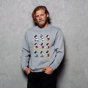 May include: A gray sweatshirt featuring a grid of nine Mickey Mouse illustrations in various poses. Mickey is depicted in black, white, red, yellow, and blue. The sweatshirt is a crew neck style.