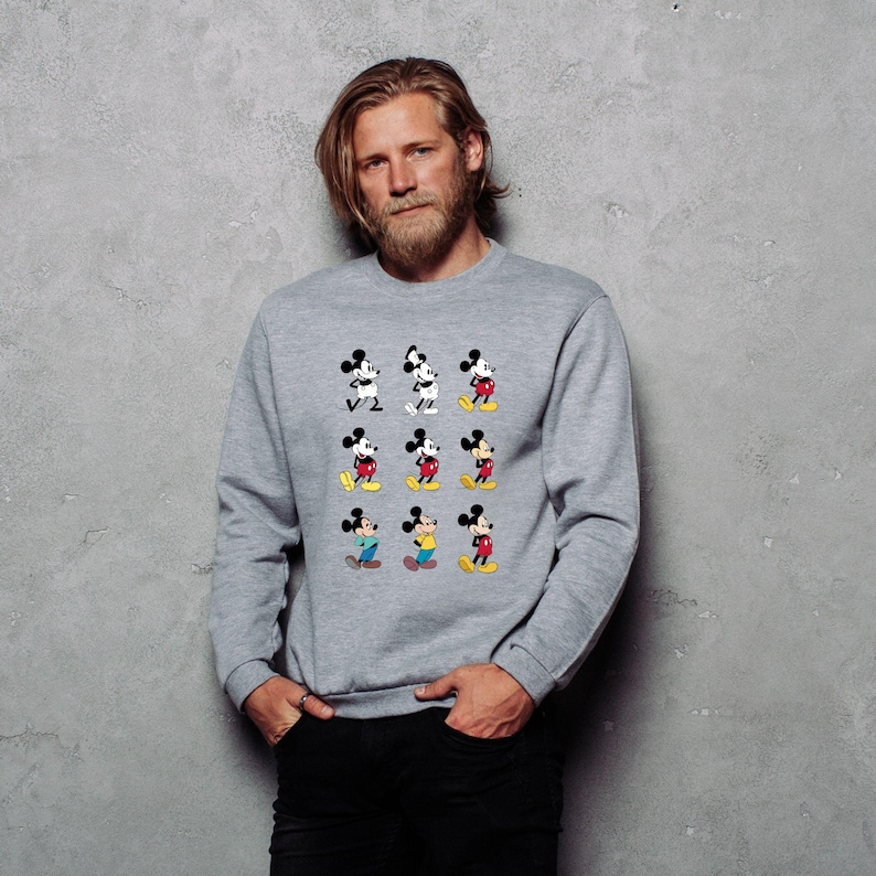 May include: A gray sweatshirt featuring a grid of nine Mickey Mouse illustrations in various poses. Mickey is depicted in black, white, red, yellow, and blue. The sweatshirt is a crew neck style.