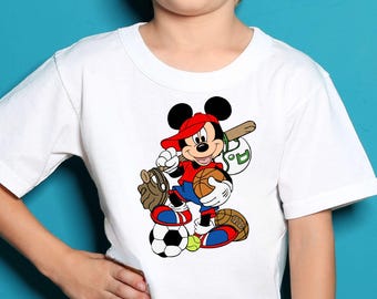Peut inclure: Un t-shirt blanc à manches courtes avec une impression graphique de Mickey Mouse portant une casquette rouge, un t-shirt rouge et un short bleu. Mickey est entouré de divers équipements sportifs dont un ballon de basket et un gant de baseball.