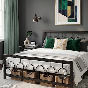 May include: A modern bedroom with a black metal bed frame featuring circular accents and woven storage baskets underneath. The bed is made with white bedding and green velvet pillows. A framed abstract art piece hangs above the bed.