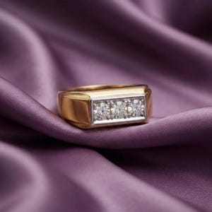 May include: A gold band ring featuring a rectangular silver-toned setting that holds three round, clear, faceted stones arranged in a horizontal row. The ring has a polished, smooth finish and a wide, solid shank design.