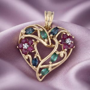 Op de afbeelding: Een hartvormige gouden hanger met twee bloemclusters met dieprode rondgeslepen stenen en kleine heldere accenten. Het ontwerp is versierd met blauwe en groene markiesgeslepen stenen die in een rankachtig patroon over het frame zijn geplaatst.