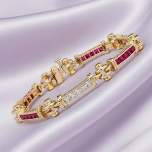 May include: A gold bracelet with alternating sections of square-cut rubies and clear, square-cut gemstones. The bracelet is set on a lavender satin surface. The clasp is visible and the bracelet is linked with gold connectors.