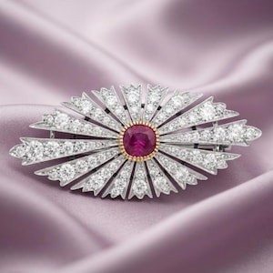 Op de afbeelding: Een zilverkleurige broche met een centrale, kussengeslepen dieprode edelsteen omringd door een goudkleurige zetting. Het sieraad is ontworpen met uitstralende, puntige stralen die bezet zijn met talloze kleine, heldere, rondgeslepen steentjes.