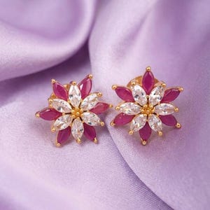 May include: A pair of gold-tone stud earrings shaped like flowers. Each earring features marquise-cut fuchsia pink stones and clear white stones arranged in a layered petal pattern, with a small gold-tone center accenting the floral design.